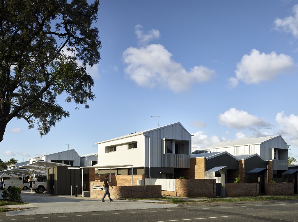 View from the street, showing the front townhouses and brick fences, and the carpark to the side.  